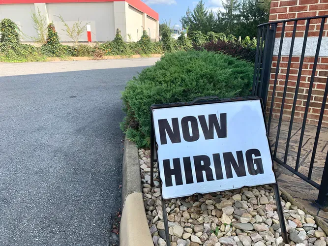A 'Now Hiring' sign in the ground.