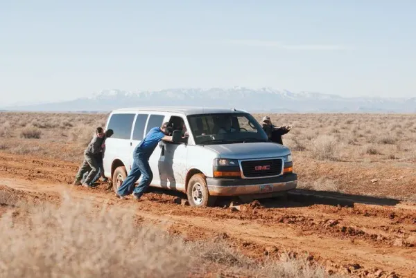 A construction team pushes their truck through a muddy road.